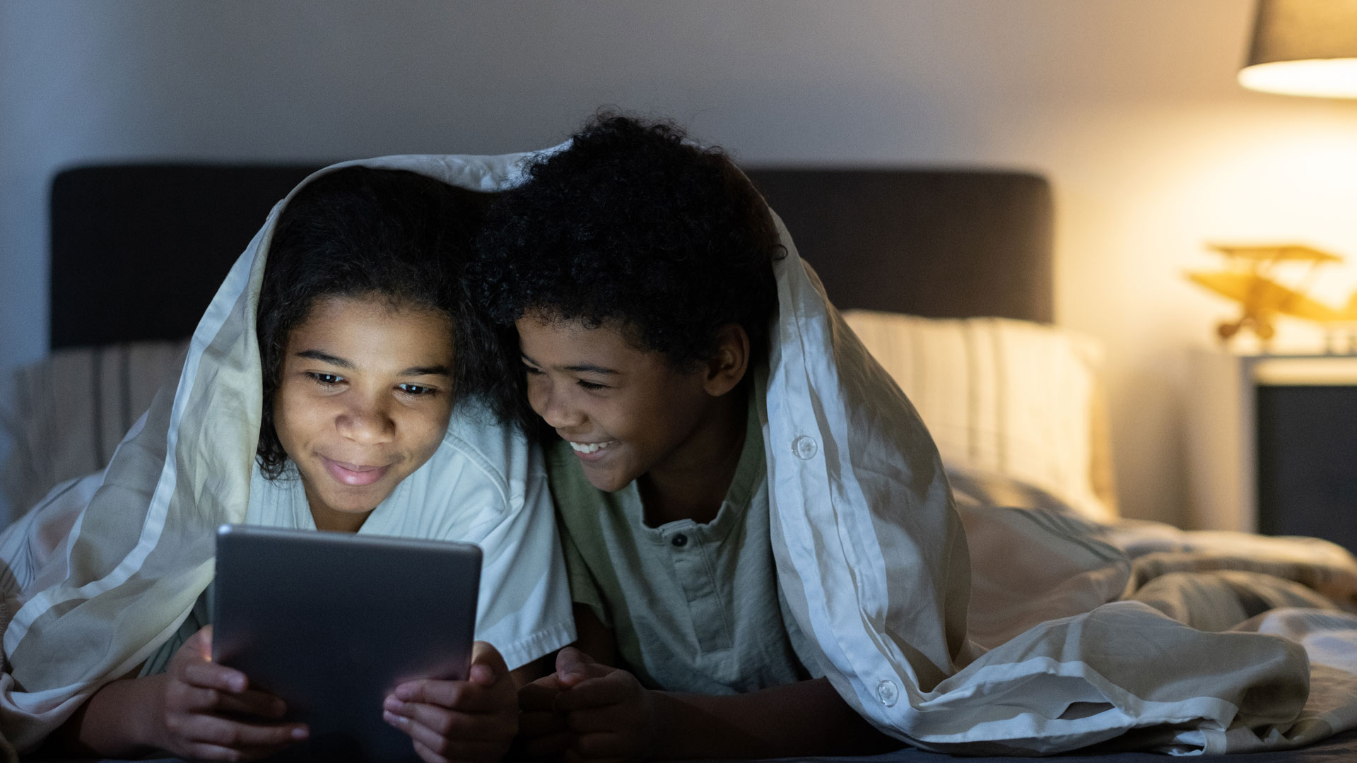 two children smiling looking at a tablet device