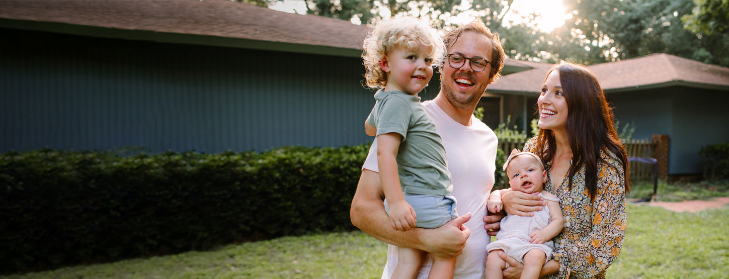 Man and a woman smiling and holding their children. 