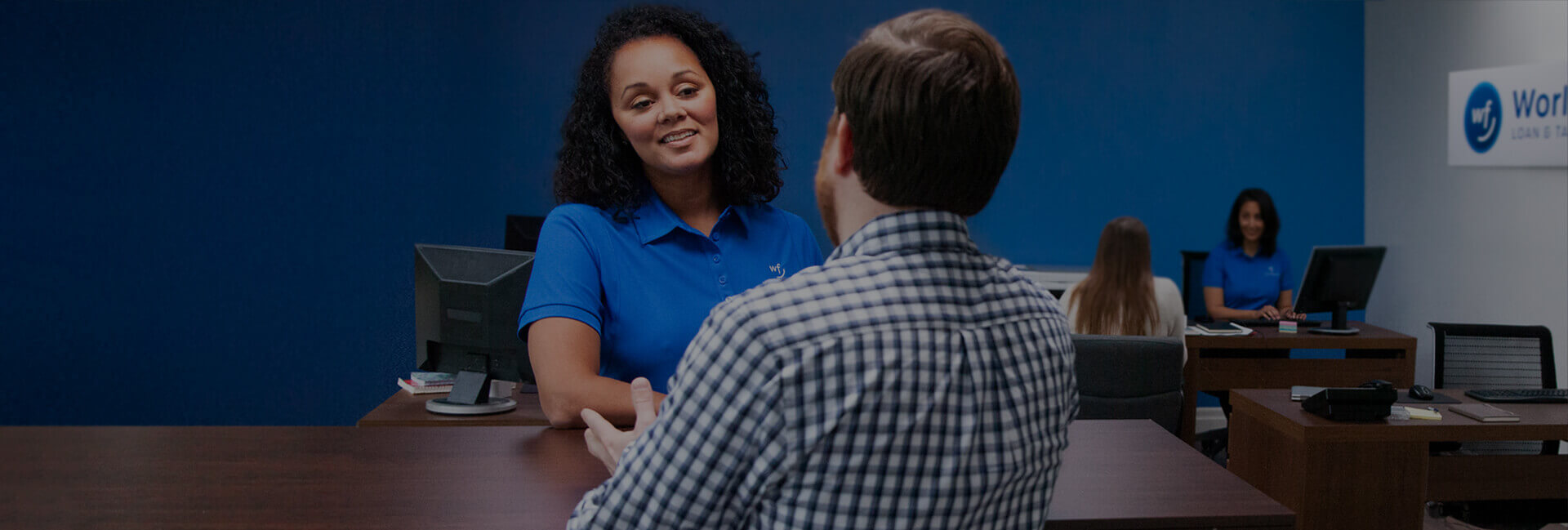 A woman with a blue 'World Finance' shirt talking across the table to a man.