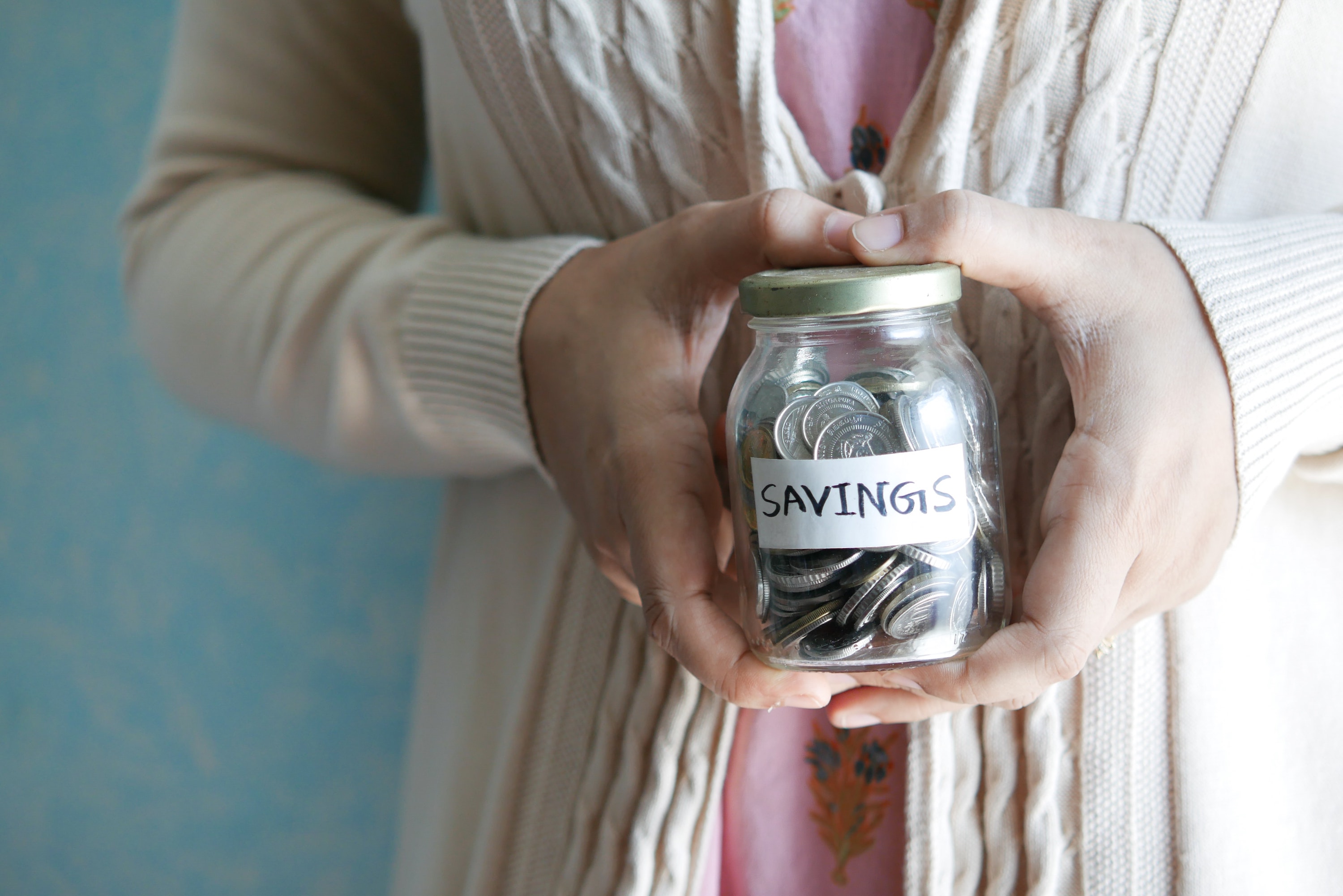 Person holding a mason jar labeled "savings" that is filled to the top with coins. 