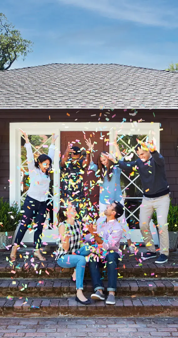 Group of people cheering in front of a house with confetti.