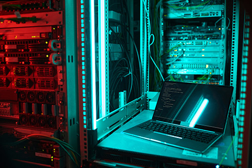 Background image of opened laptop by server cabinet in data center lit by blue light, copy space