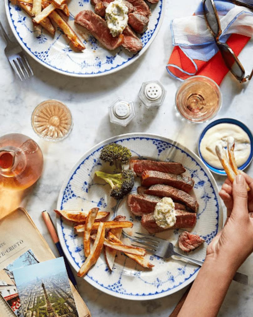 Plate of sliced steak with fries, broccoli, and dipping sauce