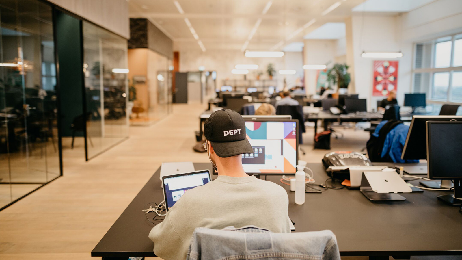 Back of man sat at a desk, wearing a black cap with DEPT logo on it.
