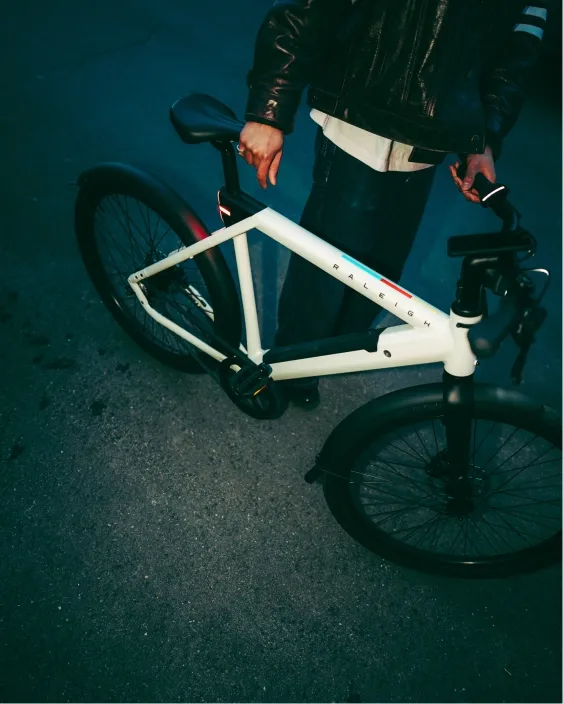 Close-up of a modern white Raleigh bicycle frame held by a person wearing a leather jacket.