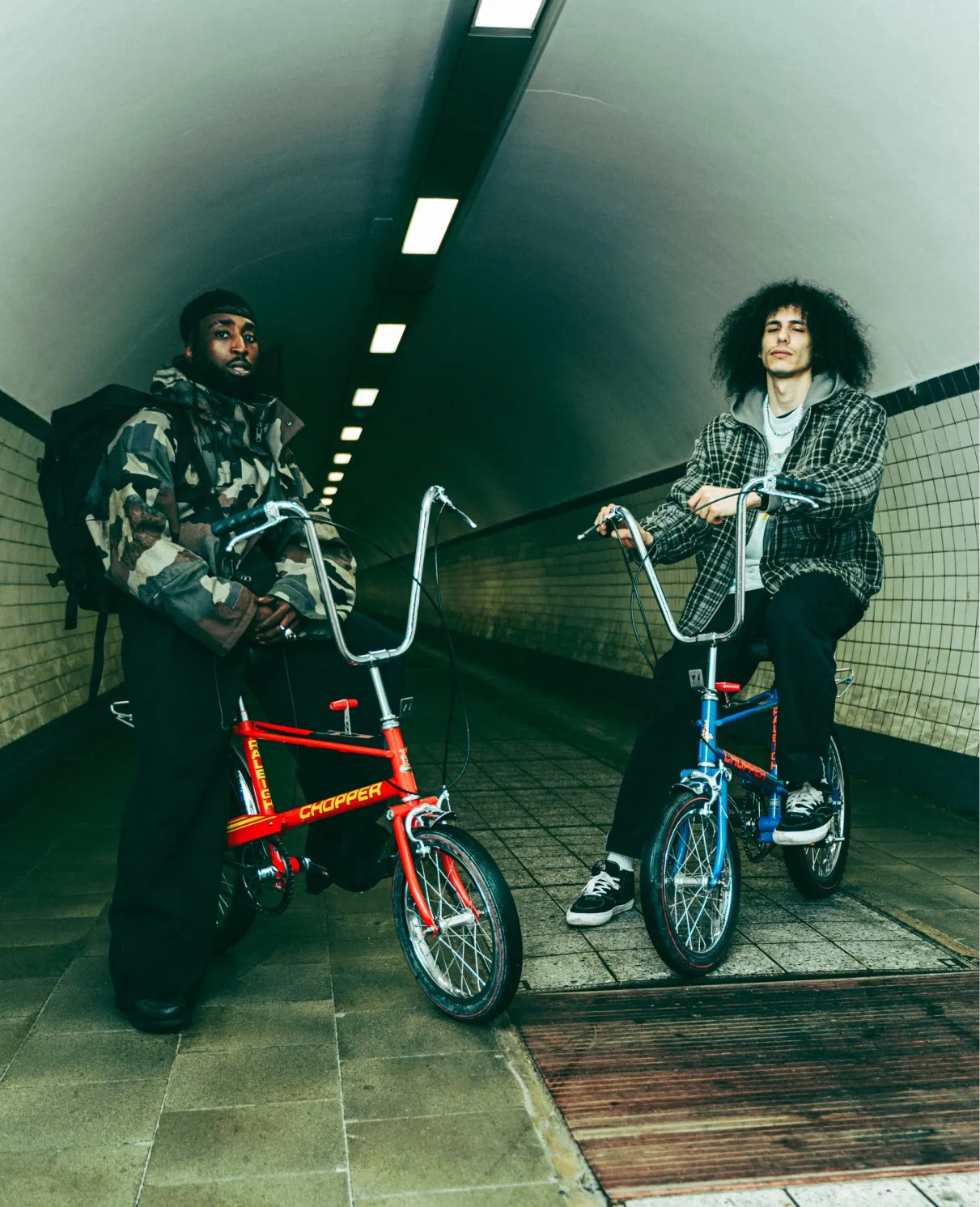 Two men on vintage Raleigh Chopper bicycles in an underground tunnel.