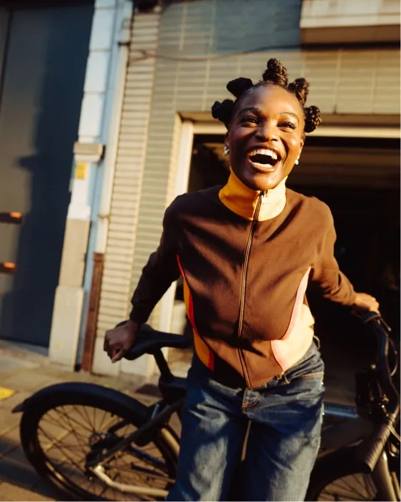 Joyful woman in a zip-up sweater standing next to a bicycle in front of a garage.