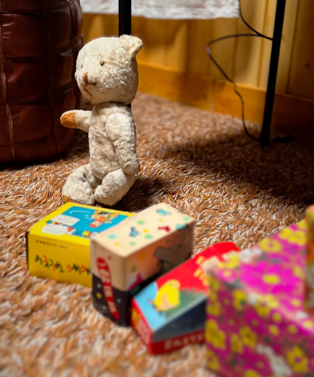 A vintage teddy bear sitting next to brightly wrapped small Christmas presents on a shag rug.